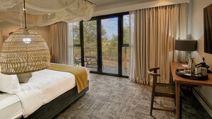 A hotel room with a bed, a hanging chair, a desk with a lamp, and a view of the outdoors through a glass door. - Cresta Marang Gardens (Francistown)