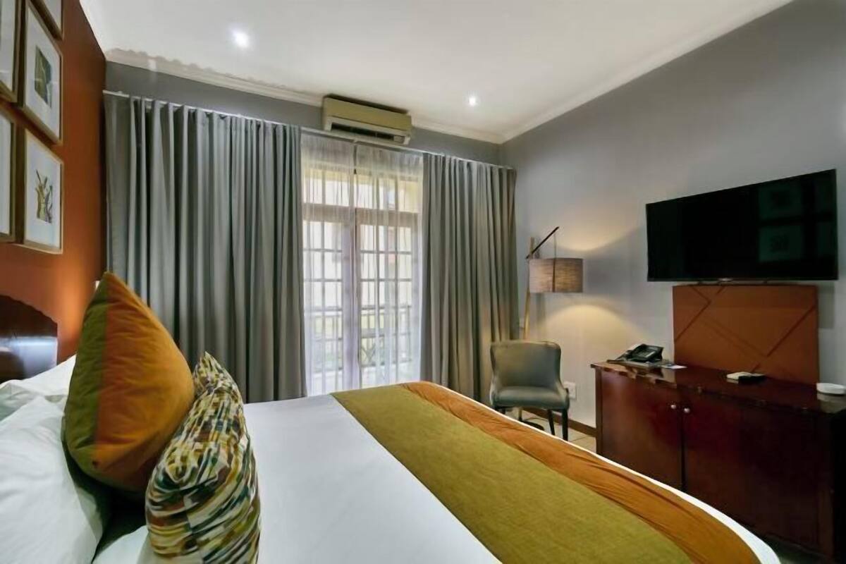 Ein Hotelzimmer mit Bett, Vorhängen, Fernseher, Schreibtisch und Stuhl.