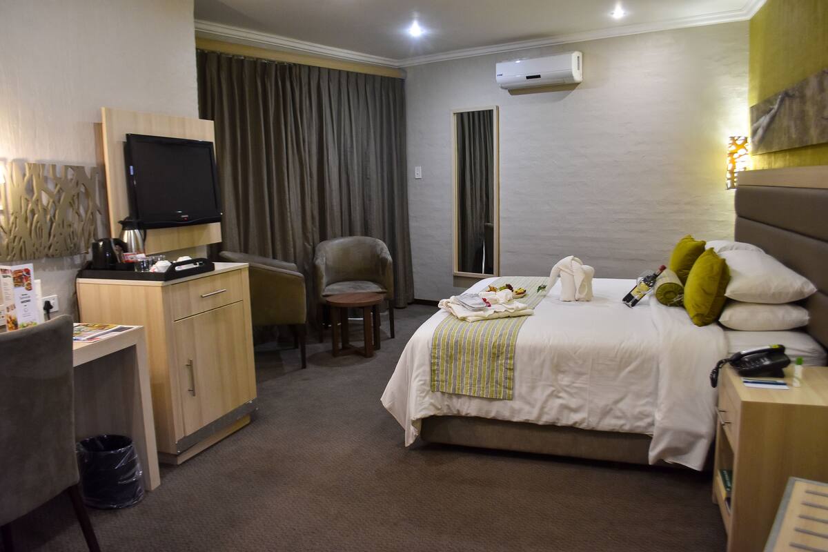 Ein Hotelzimmer mit Bett, Schreibtisch, Stuhl, Fernseher und Klimaanlage.
