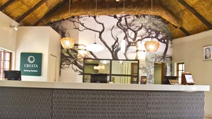 A reception desk with a modern design, a mural of trees on the wall, and a ceiling with a wooden beam structure. - Cresta Marang Gardens (Francistown)