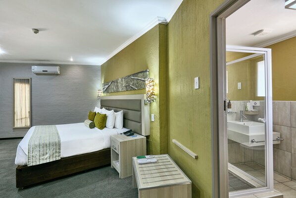 Una habitación de hotel con cama, mesita de noche y baño con lavabo y espejo.