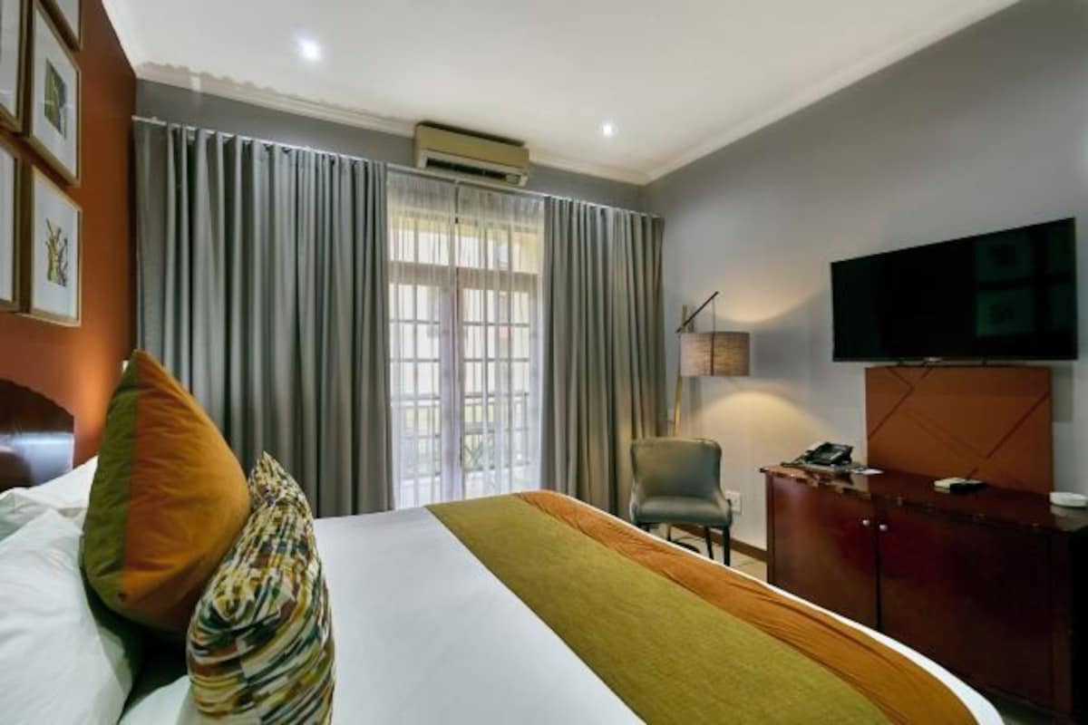 A hotel room with a bed, curtains, a TV, a desk, and a chair.
