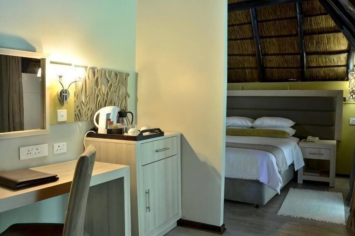 Ein Hotelzimmer mit Schreibtisch, Stuhl, Bett und einem durch das Fenster sichtbaren Reetdach.