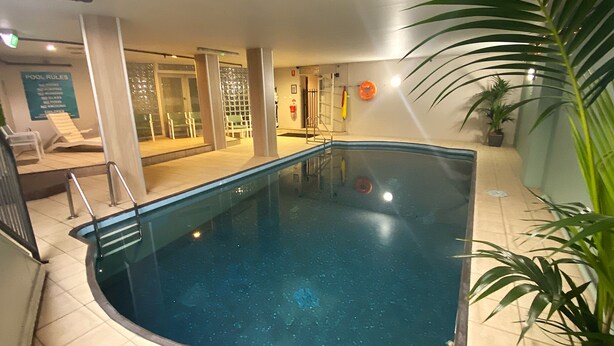A swimming pool with a tiled floor, a poolside area with chairs, and a sign indicating pool rules. - Adelaide Royal Coach (Kent Town)