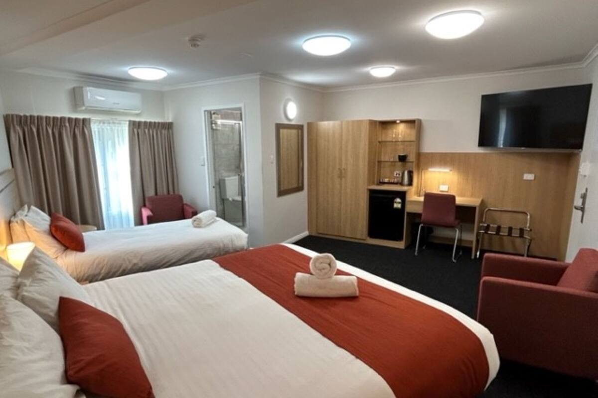 A hotel room with two beds, a desk, a TV, and a kitchenette.