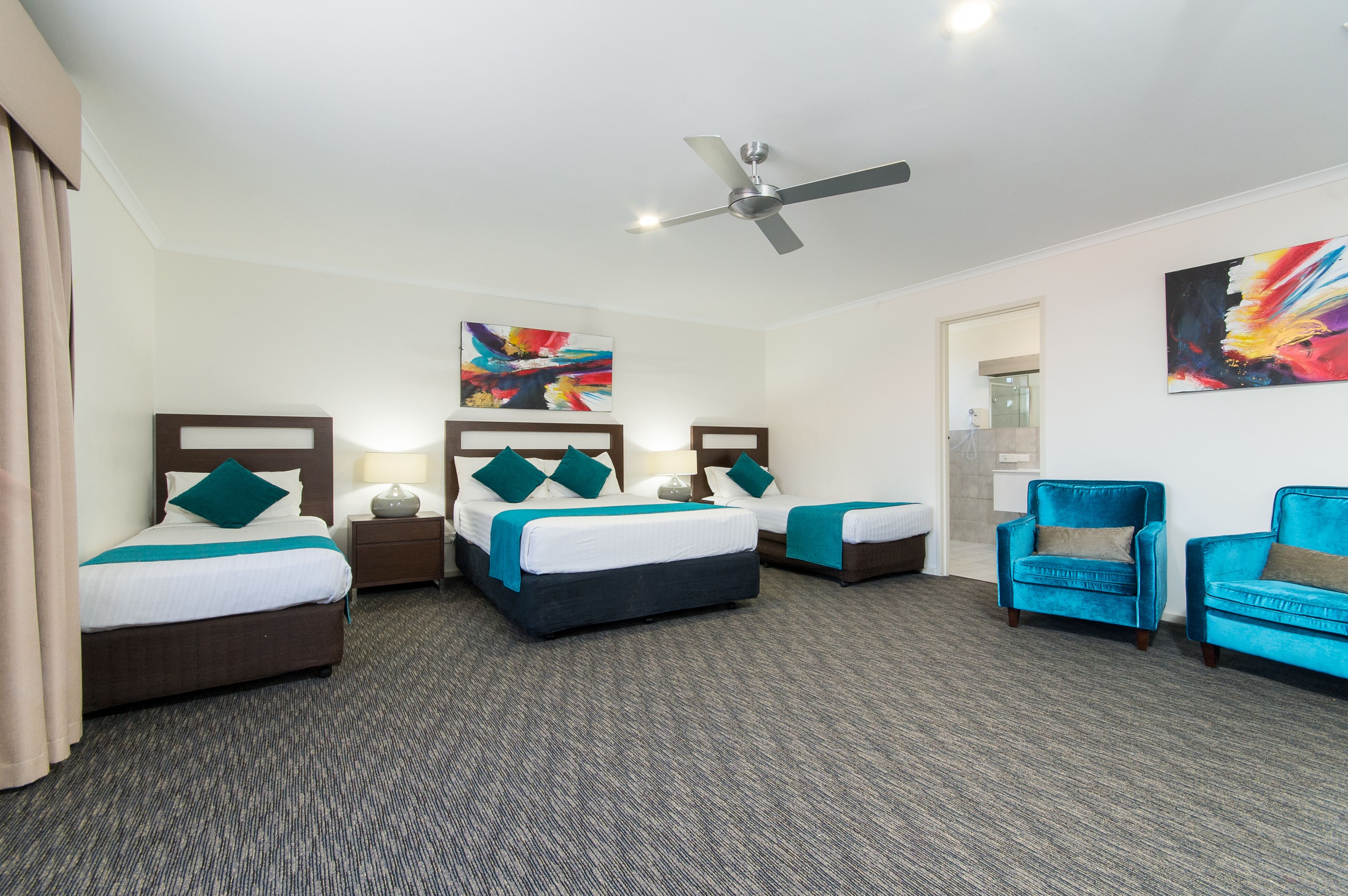Habitación de hotel con dos camas, un ventilador de techo y dos sillones azules.