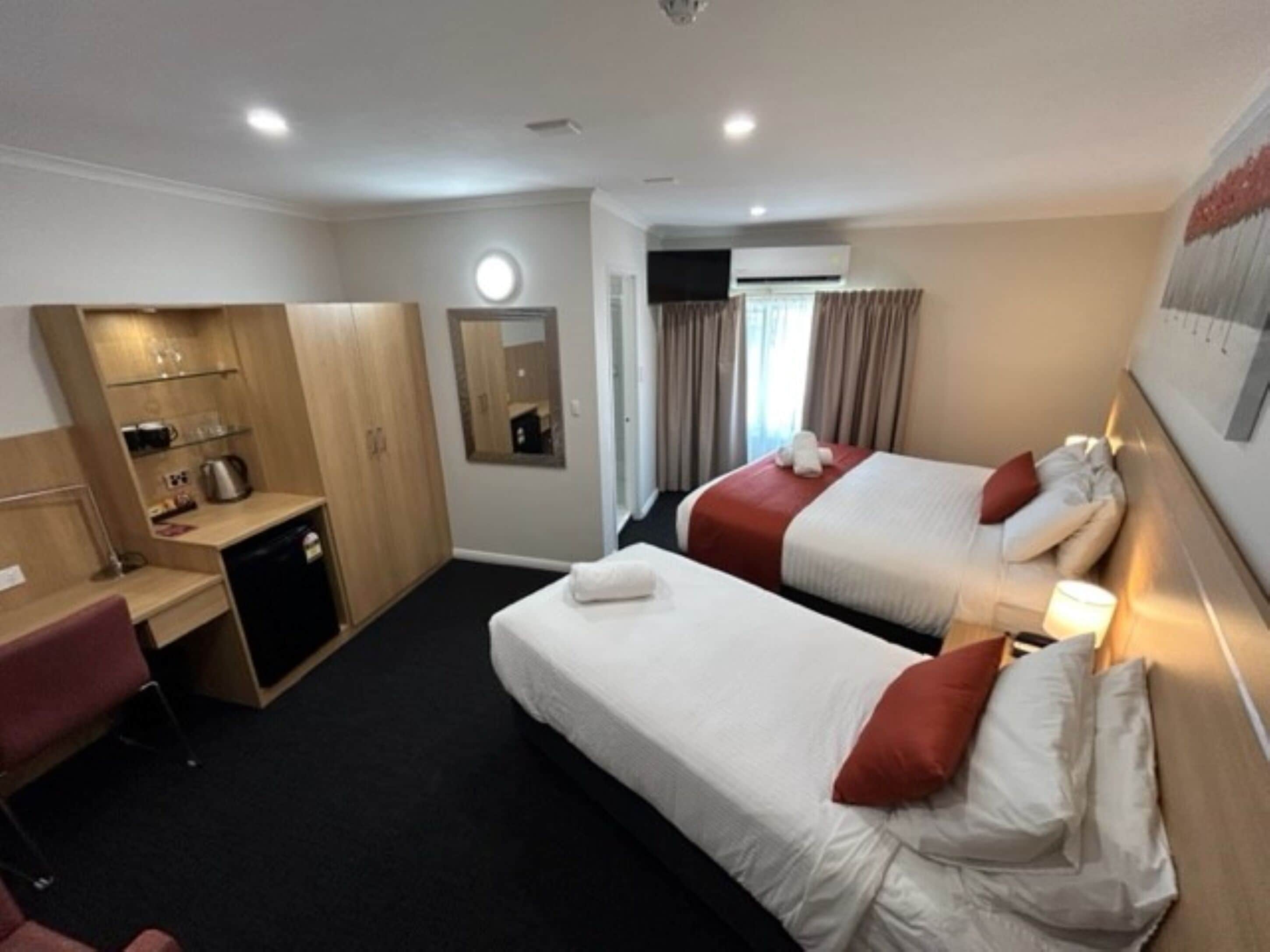 A hotel room with two single beds, a desk with a chair, a wardrobe, and a mirror.