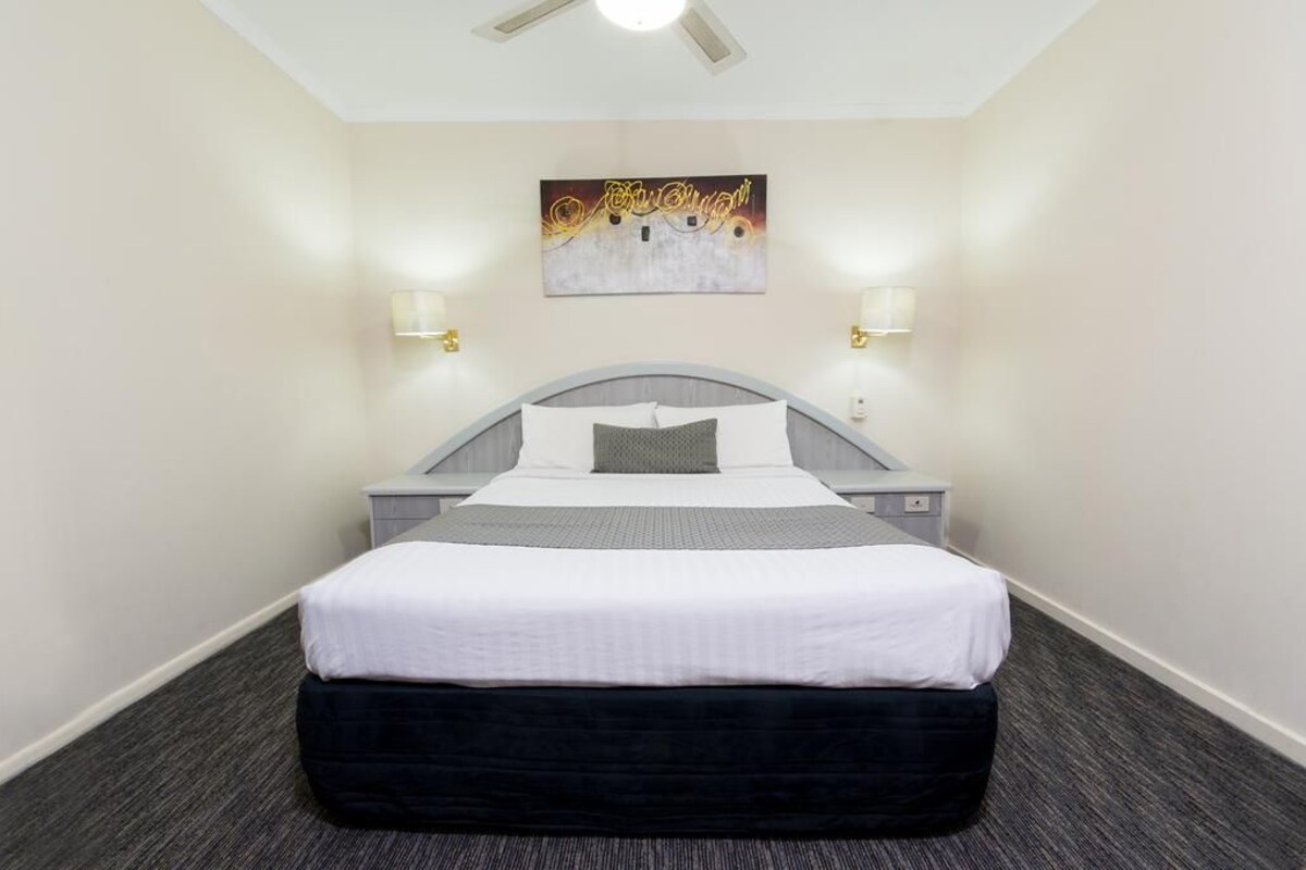 Habitación de hotel con cama, mesitas de noche, una obra de arte colgada en la pared y dos lámparas de pared.