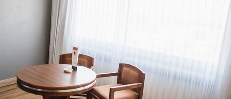 Una habitación con una mesa redonda de madera y dos sillas de madera, una cortina blanca y suelo de madera.