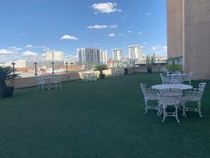 Una terraza en la azotea con césped artificial, mesas y sillas de metal blanco y plantas en macetas.