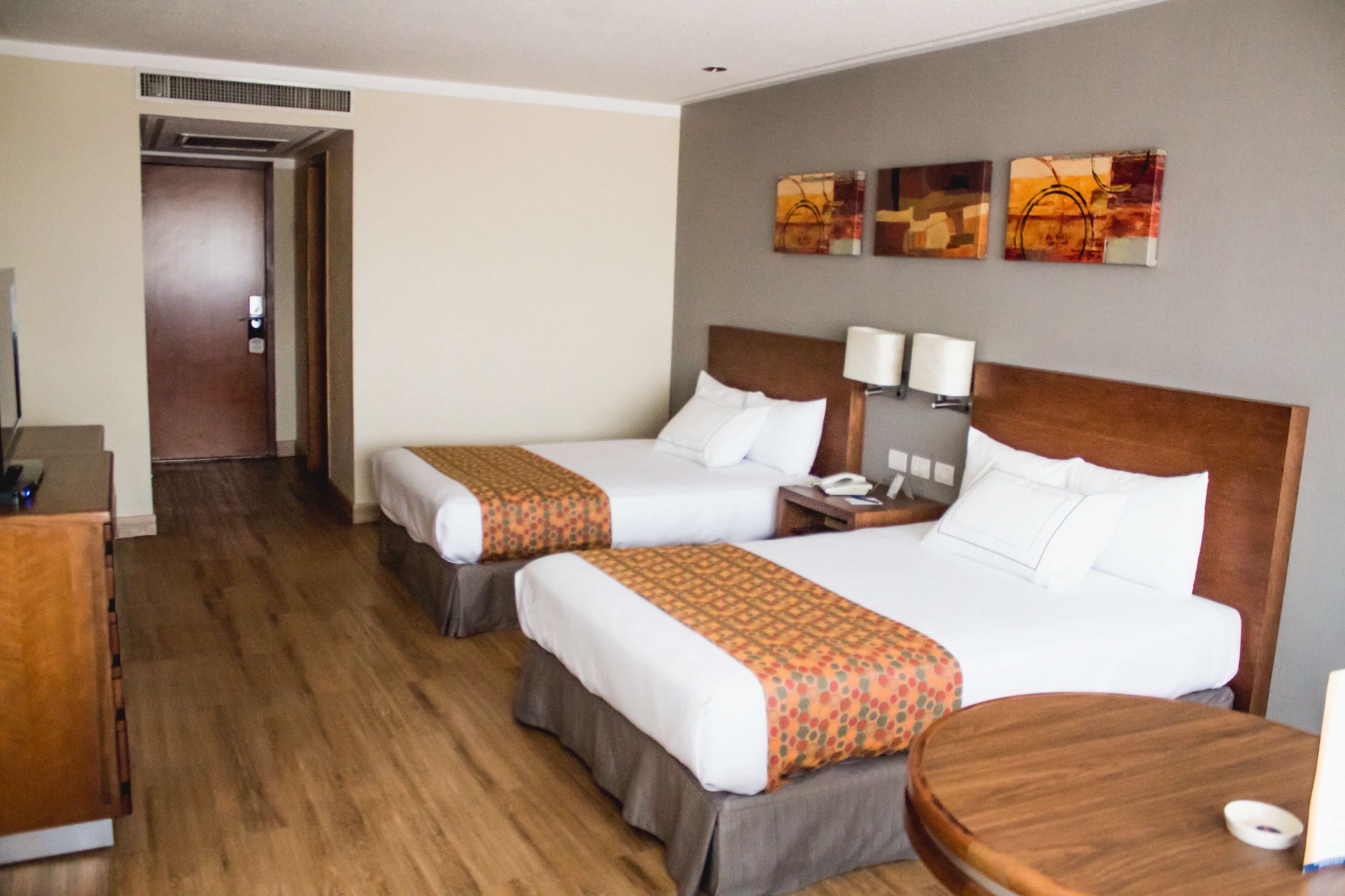 A hotel room with two beds, wooden flooring, a desk, and a small round table.