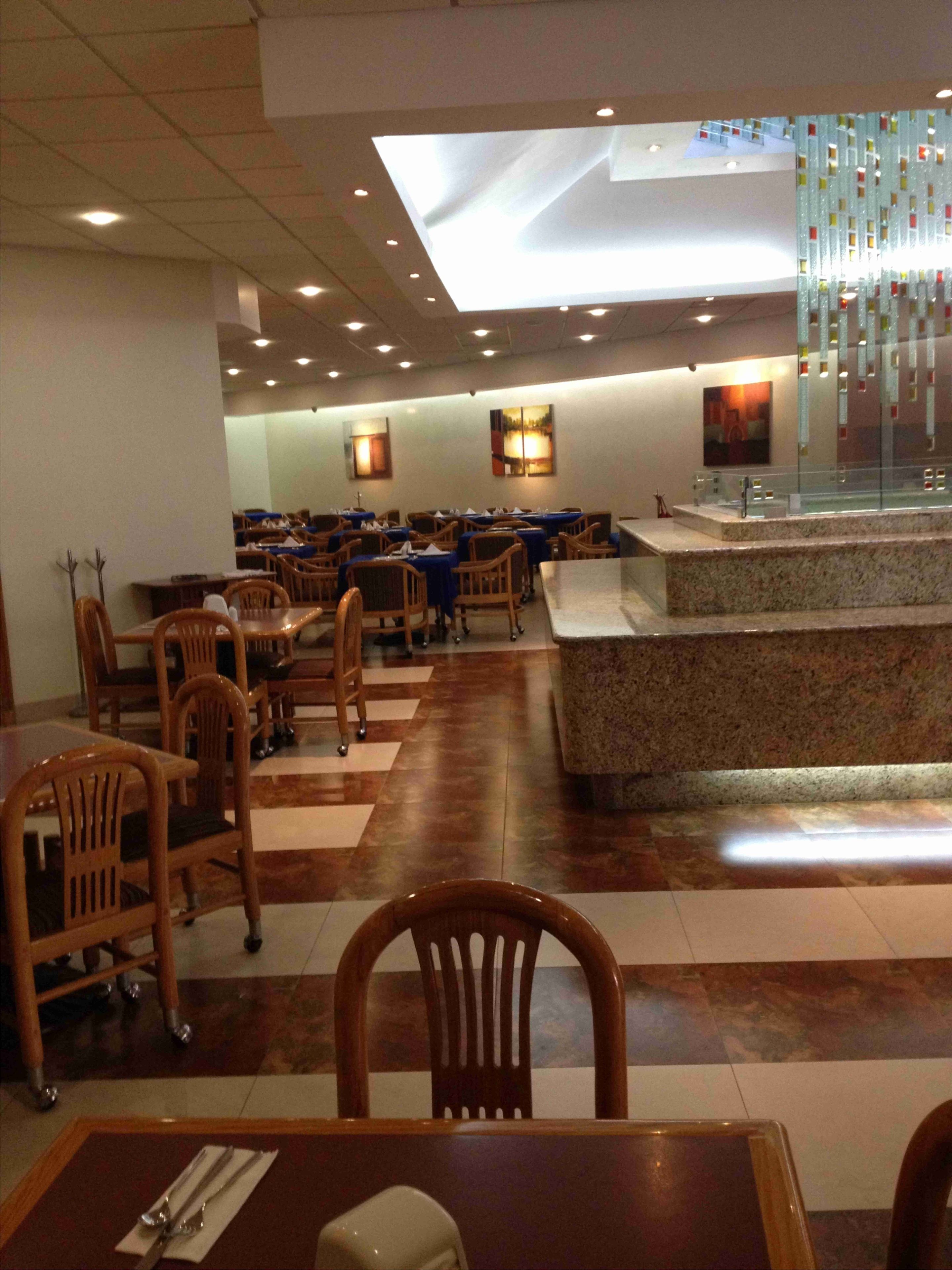 A spacious dining area with multiple tables and chairs, a central counter, and a modern ceiling design.