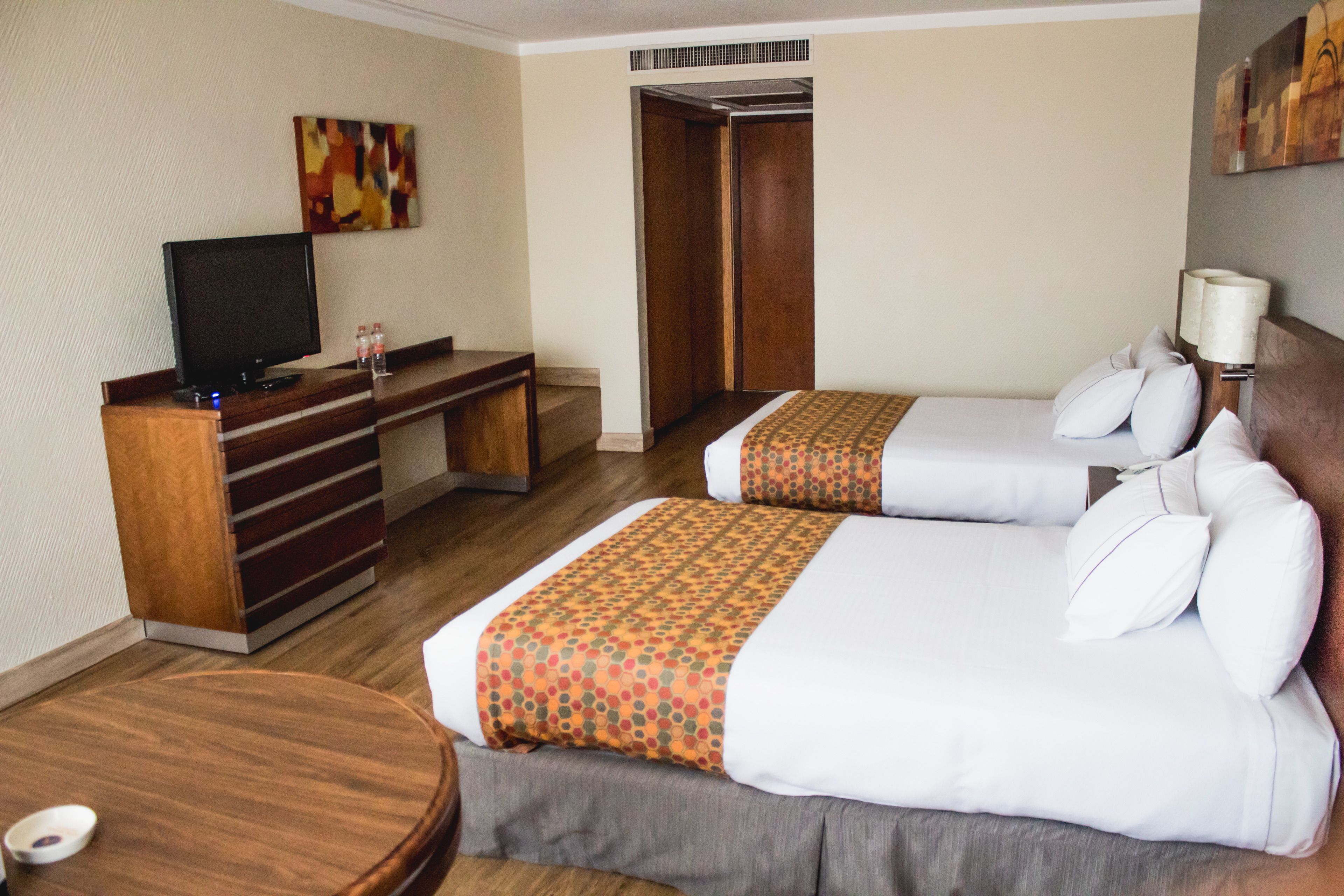 Habitación de hotel con dos camas, un escritorio con televisor y un armario.