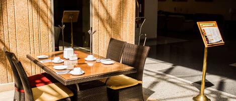 A dining area with a table set for four, surrounded by wicker chairs, in a well-lit room with a view of the outside.
