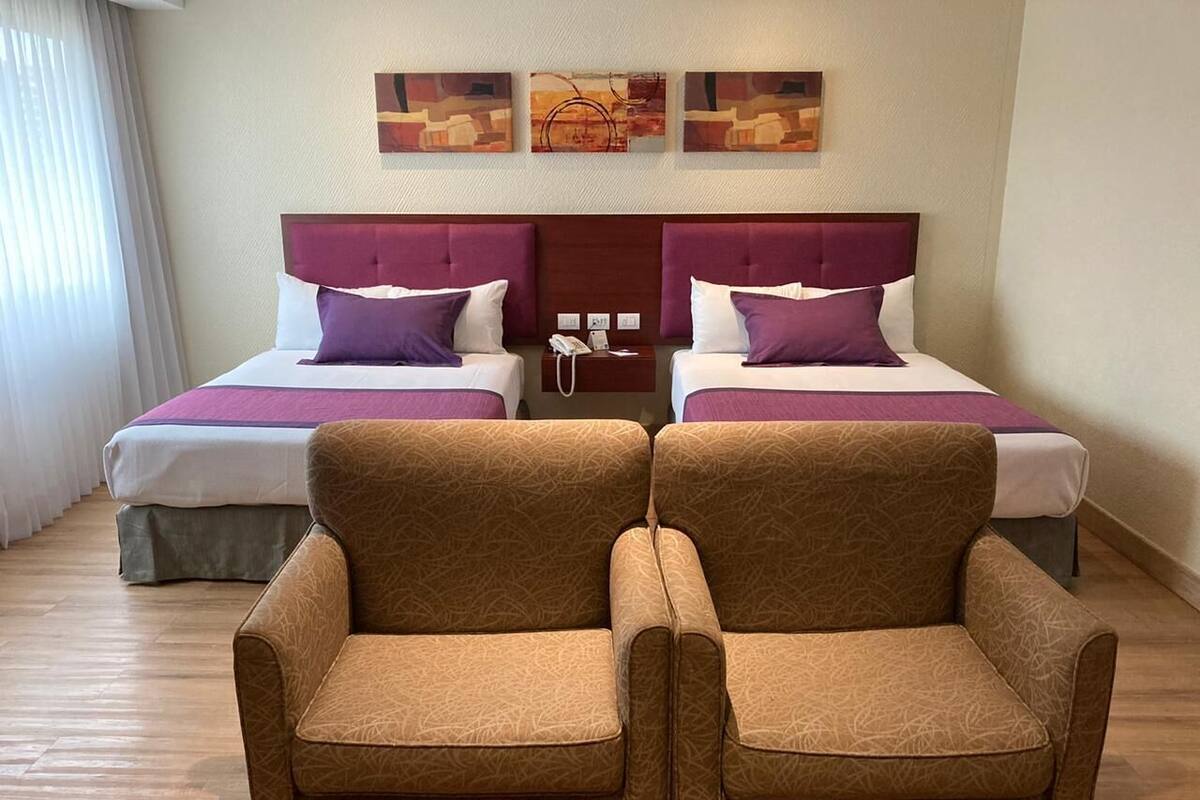 Habitación de hotel con dos camas, suelo de madera y dos sillones.