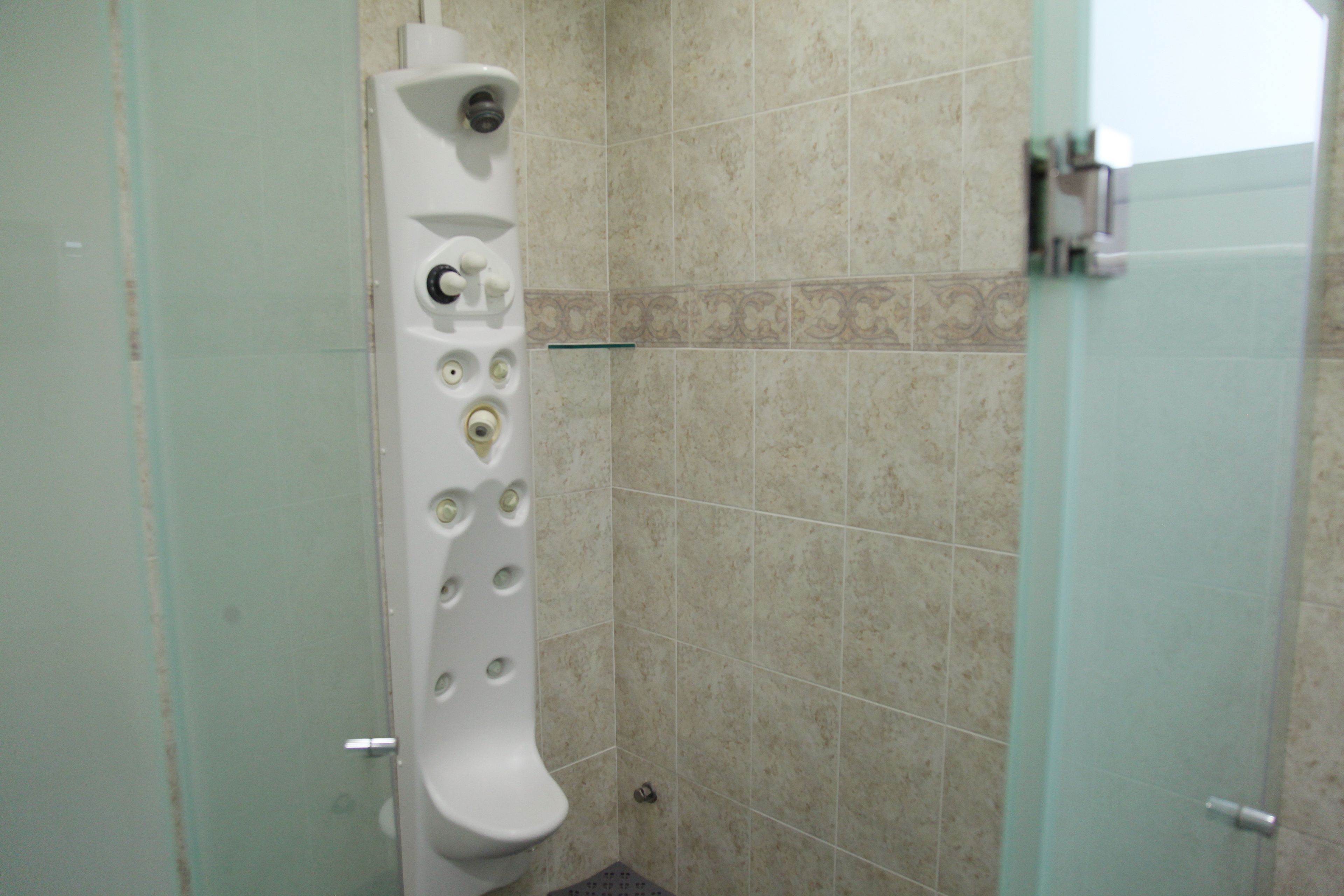 A bathroom with a white toilet, a glass shower enclosure, and beige tiled walls.