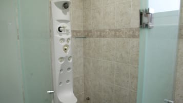 A bathroom with a white toilet, a glass shower enclosure, and beige tiled walls.