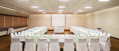 A conference room with a long table, white chairs, and a projector screen.