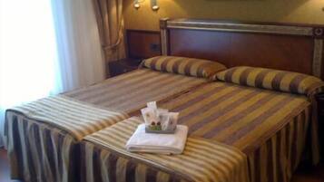 Habitación de hotel con cama doble, ropa de cama a rayas, mesita de noche con lámparas y un cuadro en la pared.