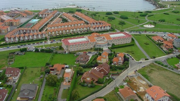 An aerial view of a coastal residential area with a large building complex, green spaces, and a marina. - Begoña Park (Gijon)