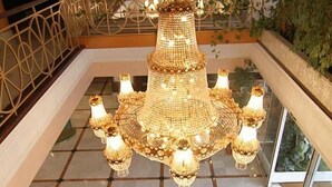 A grand chandelier with multiple tiers and lights, a patterned rug, and a small table with a floral arrangement in a spacious lobby with tiled flooring and a glass railing. - Begoña Park (Gijon)