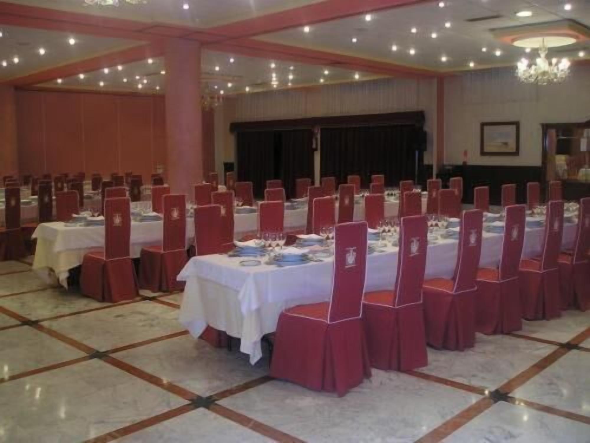 Un salón de banquetes con mesas dispuestas para un evento formal, que cuenta con piso de mármol y sillas rojas.
