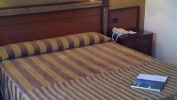 Ein Hotelzimmer mit einem hölzernen Kopfteil, einer gestreiften Bettdecke, zwei Nachttischlampen, einem gerahmten Bild an der Wand und einem Telefontisch.