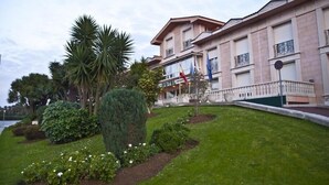A hotel with a well-maintained lawn, palm trees, and a flagpole. - Begoña Park (Gijon)