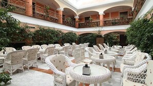 A spacious indoor courtyard with multiple wicker tables and chairs, surrounded by arches and columns, and lush greenery. - Begoña Park (Gijon)