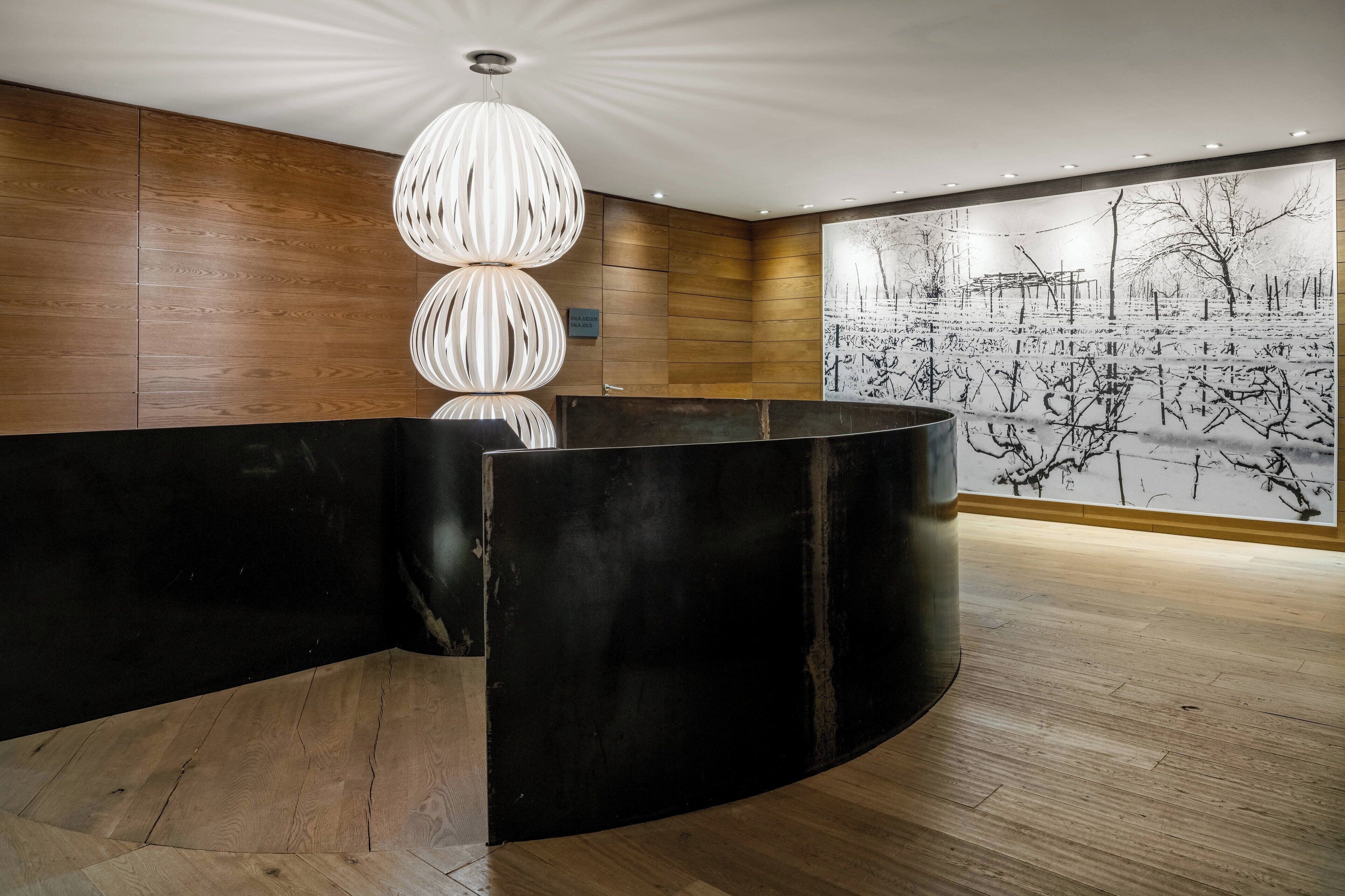 Un espace d’accueil doté d’un comptoir de réception noir incurvé, de murs recouverts de panneaux en bois et d’une grande œuvre d’art en noir et blanc représentant un paysage hivernal.