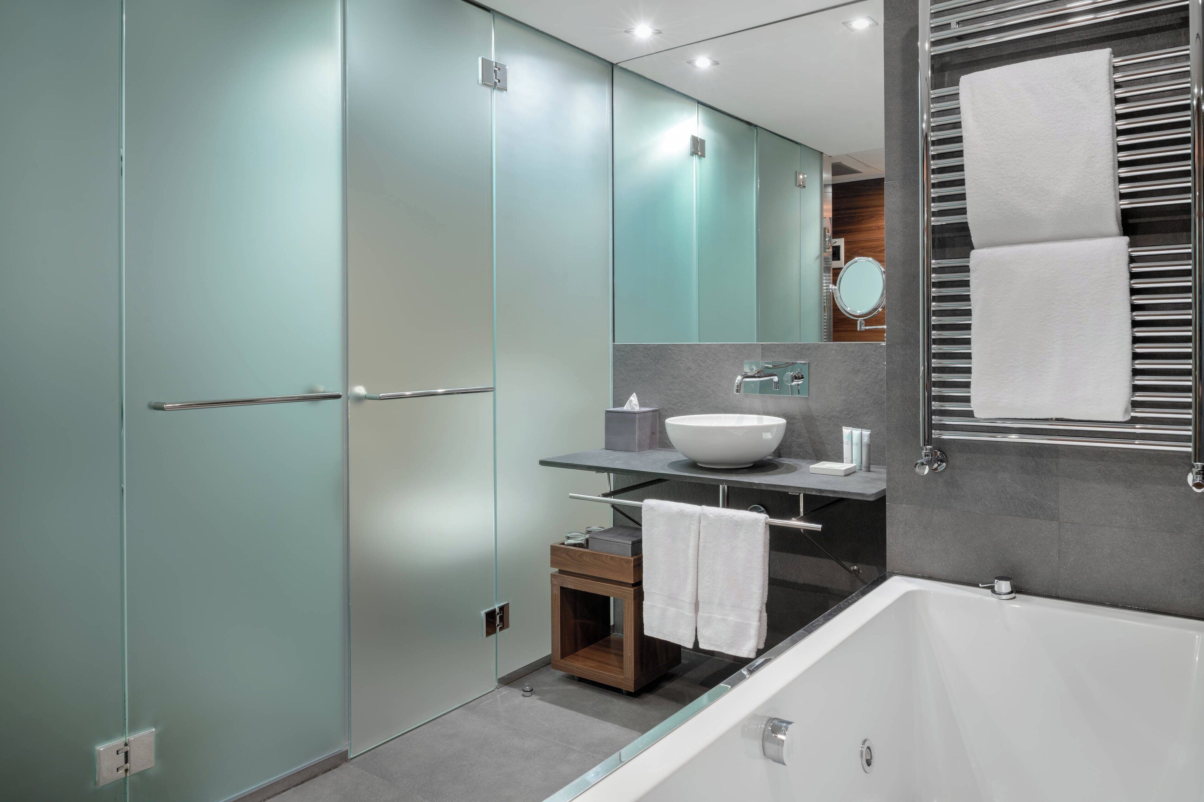 Un baño moderno con cabina de ducha de vidrio, una bañera independiente, un tocador con un espejo grande y un perchero para toallas.