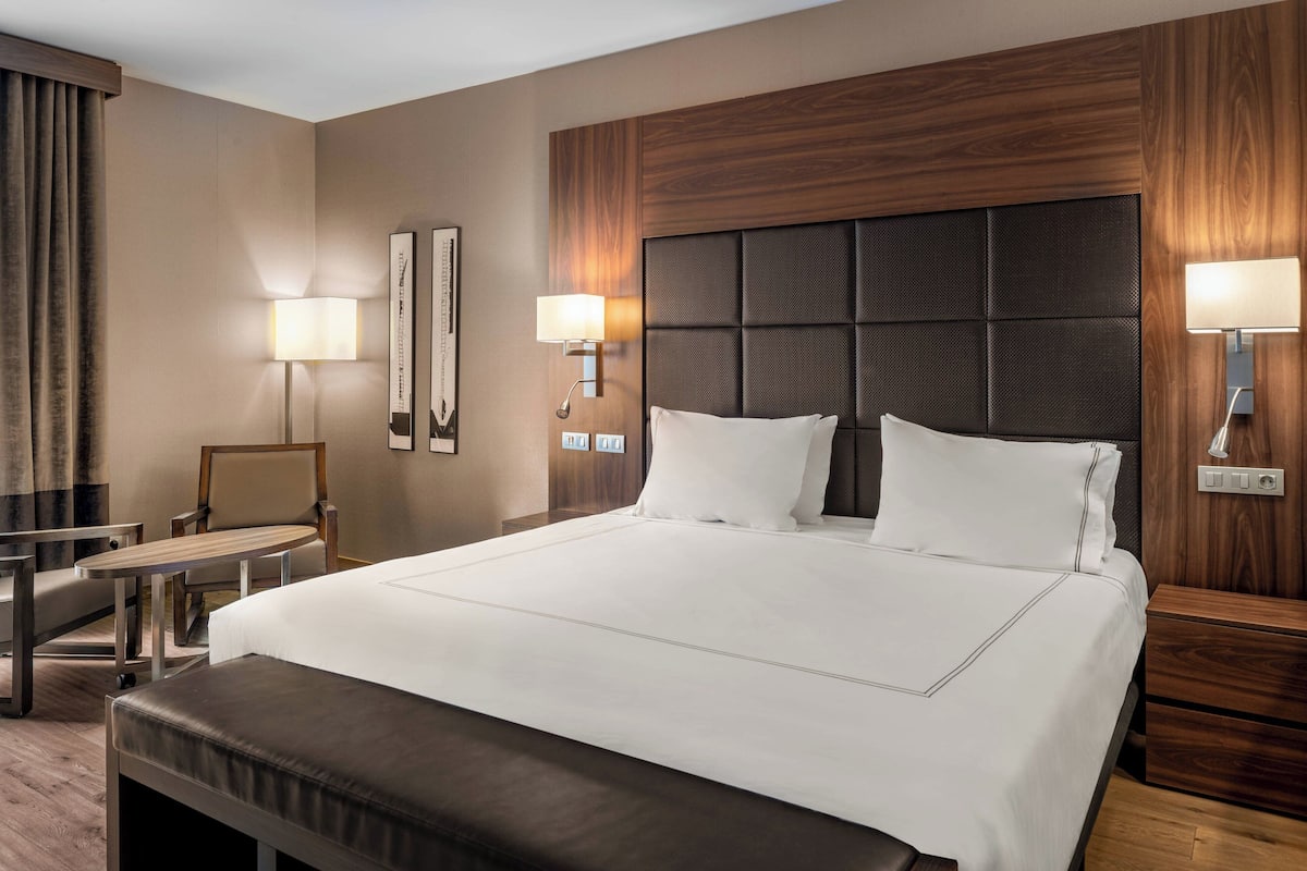 Ein Hotelzimmer mit einem großen Bett, zwei Nachttischen, einem Sessel und zwei Wandlampen.