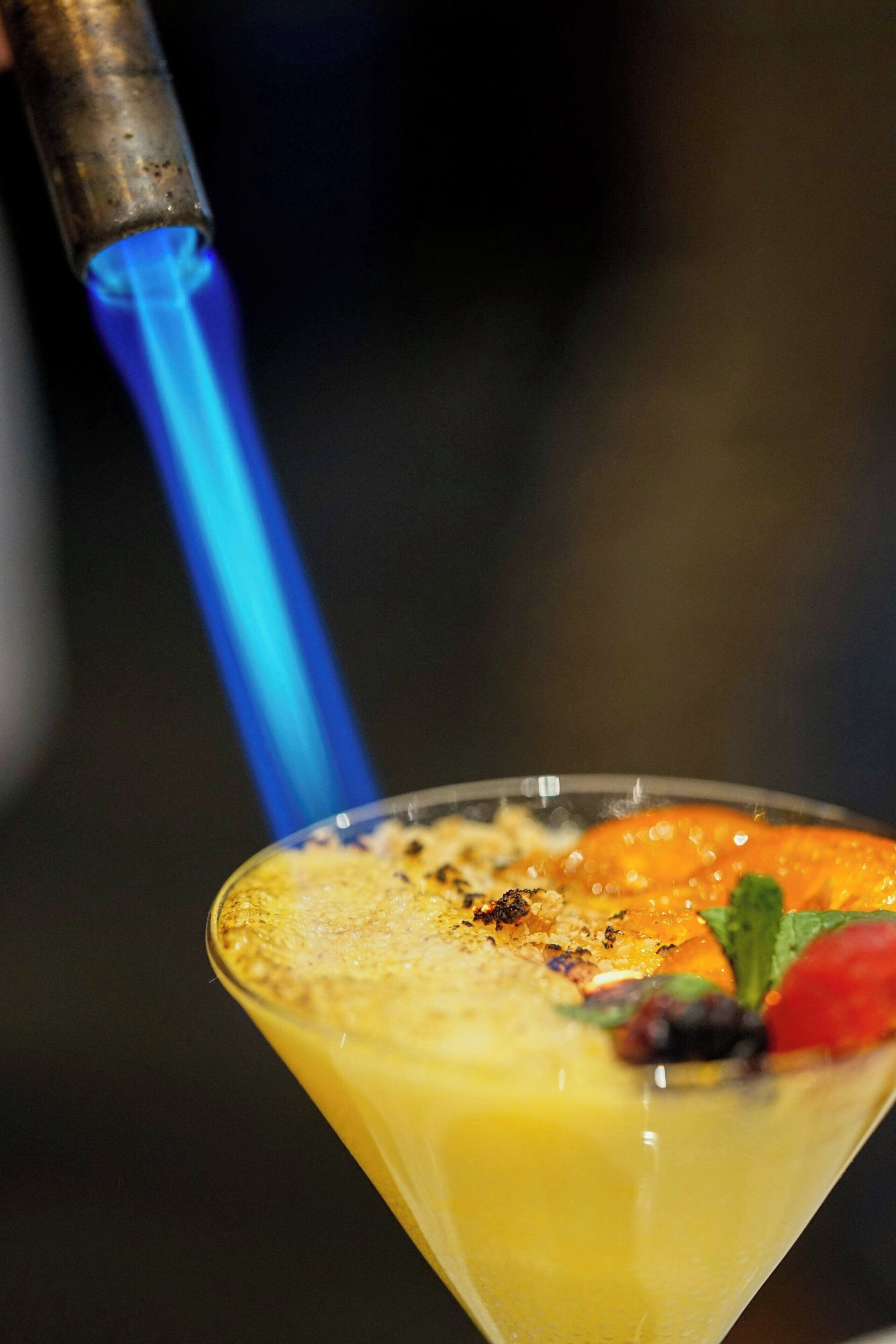 A cocktail in a martini glass with a blue flame above it.