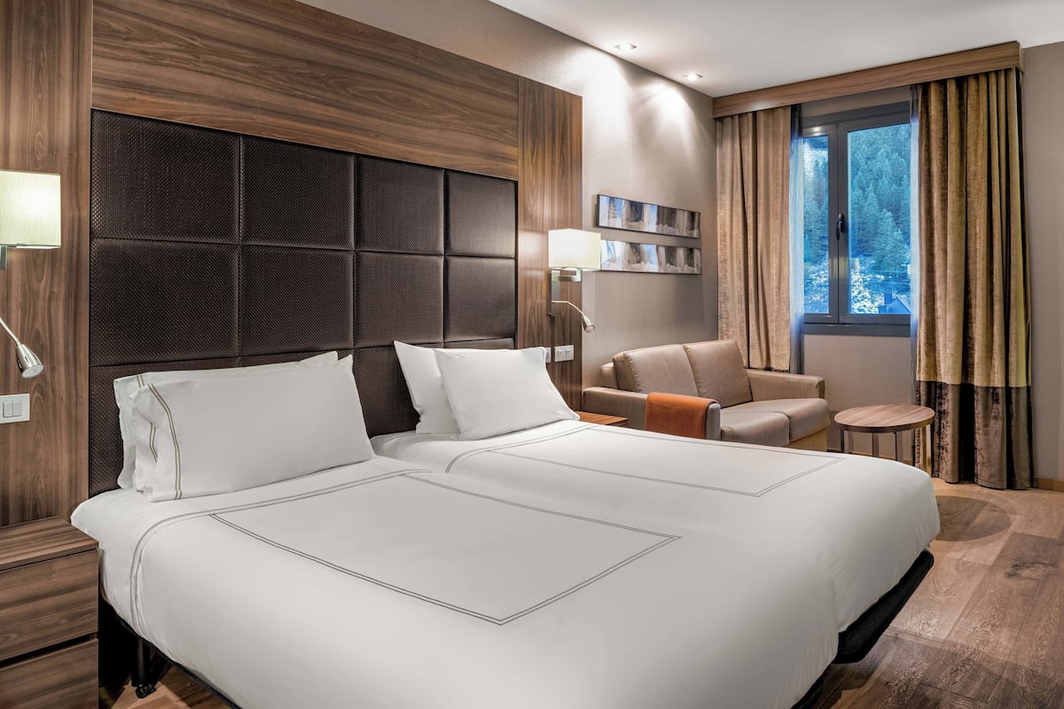Ein Hotelzimmer mit einem großen Bett, einer Sitzecke inklusive Sofa und Sesseln, einem kleinen Tisch und einem Fenster mit Vorhängen.