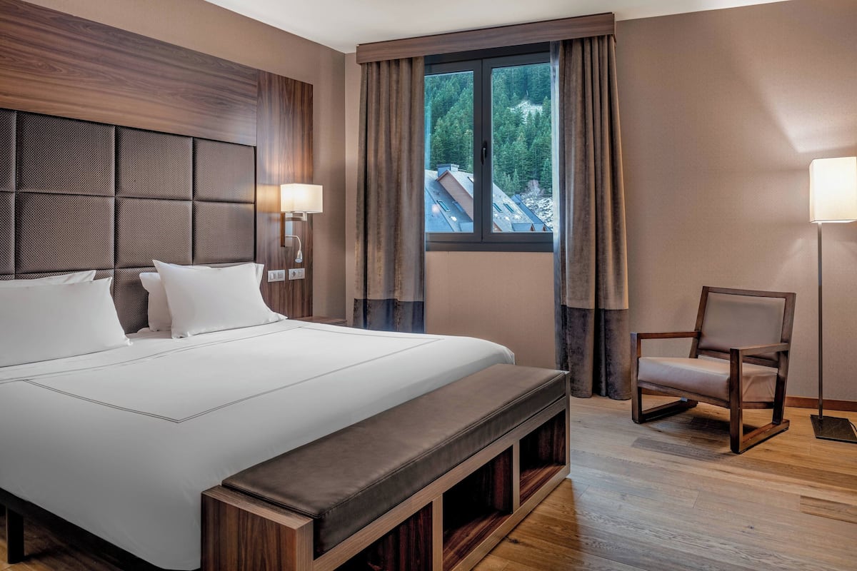 Ein Hotelzimmer mit einem großen Bett, einem Holzkopfschild, zwei Nachttischlampen, einem Fenster mit Vorhängen und einem Sessel.