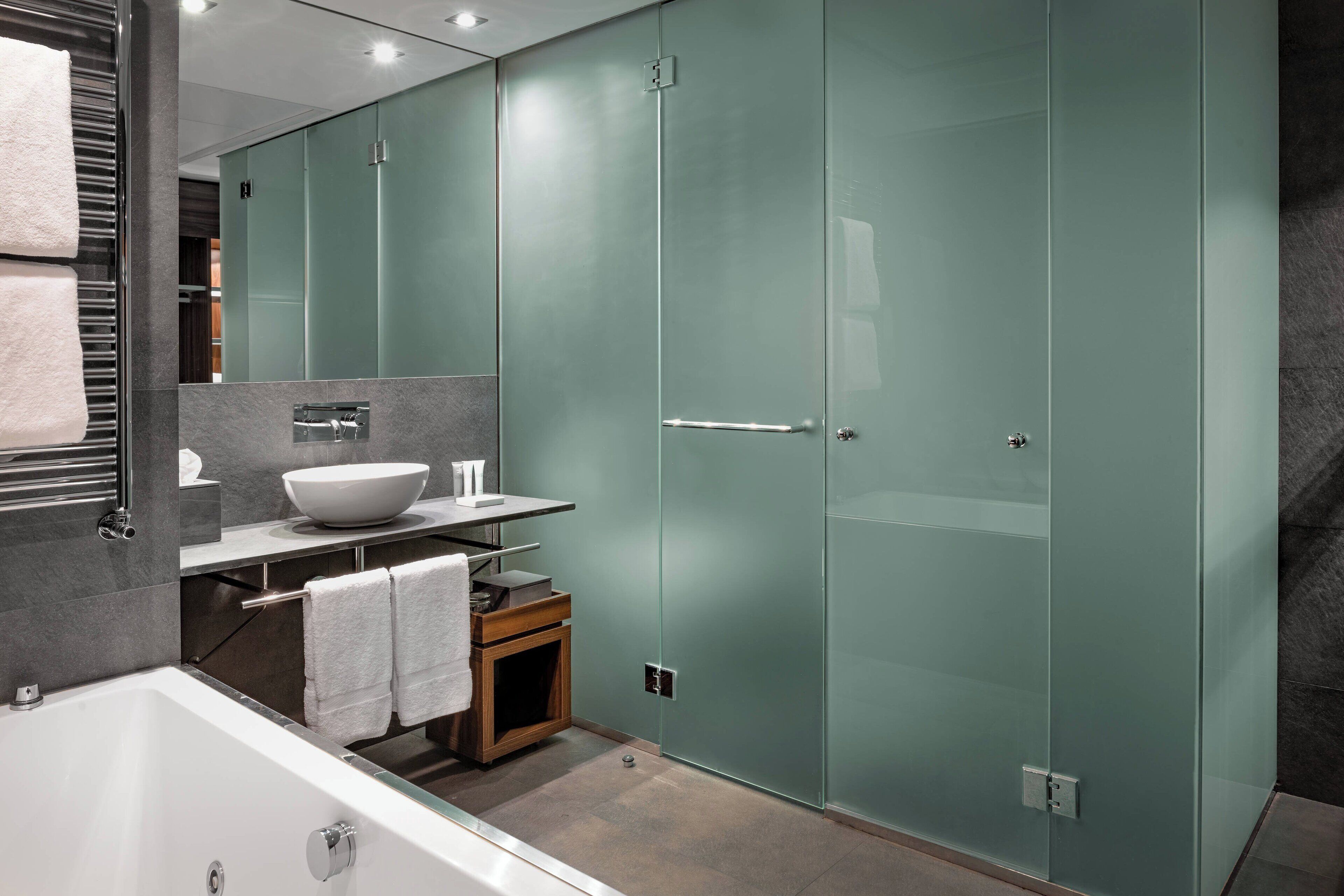 A modern bathroom with a glass shower enclosure, a white bathtub, and a vanity with a bowl sink.