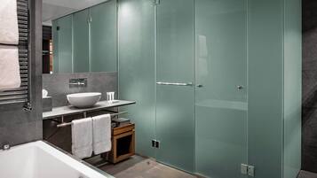 A modern bathroom with a glass shower enclosure, a white bathtub, and a vanity with a bowl sink.