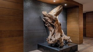 Un intérieur moderne avec un plancher en bois, un mur texturé de couleur sombre et une grande sculpture en bois posée sur un piédestal noir.