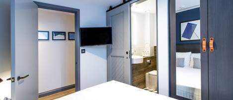 Un dormitorio moderno con una cama grande, un televisor montado en la pared, un armario con puerta corredera y un baño visible a través de una puerta abierta.