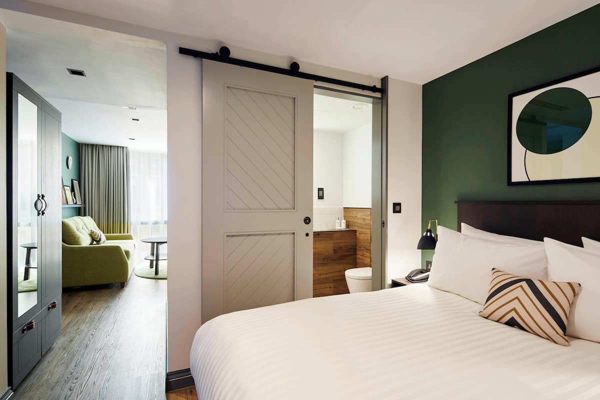 A hotel room with a bed, a green sofa, a bathroom, and a sliding door.