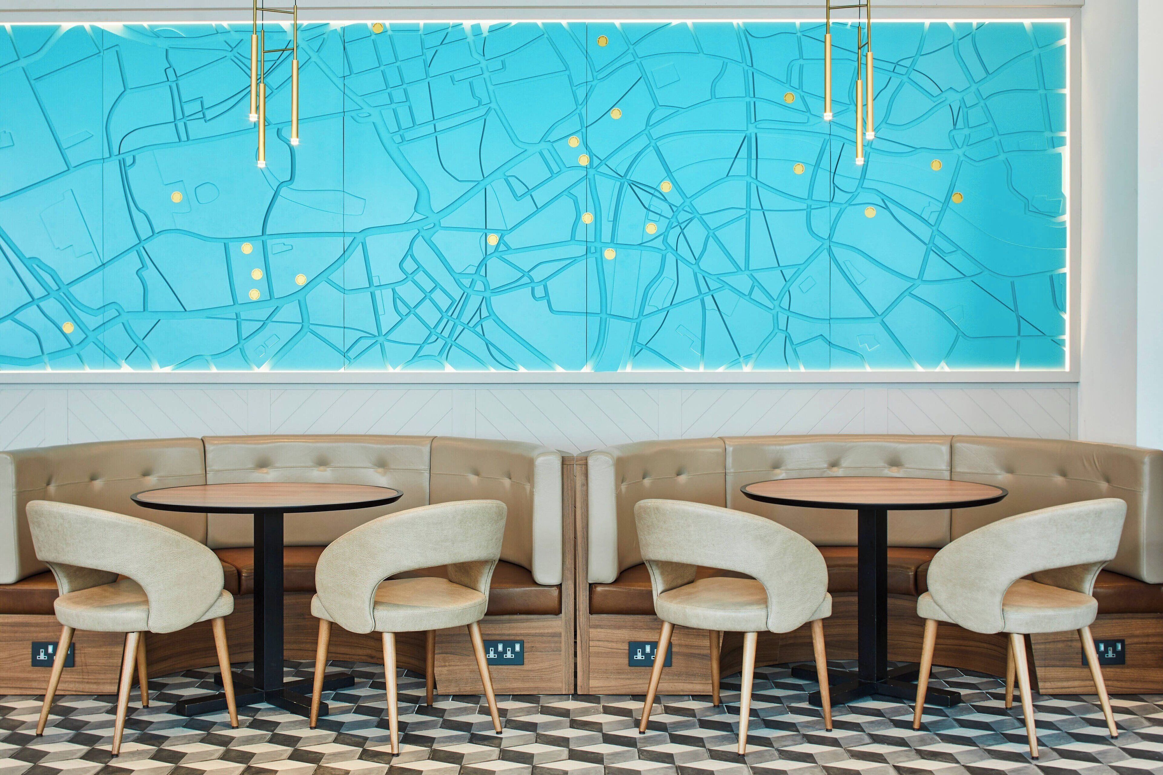 A restaurant with a large blue map mural, two round tables with chairs, and a check-in station.