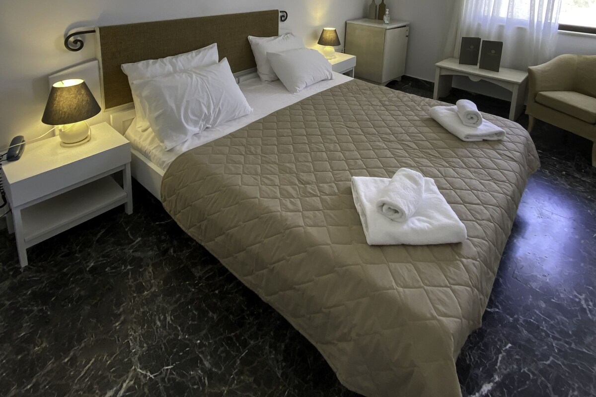 Una habitación de hotel con cama, mesitas de noche, lámpara, silla y aire acondicionado.
