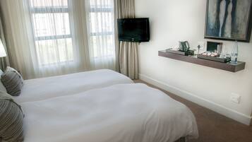 Habitación de hotel con dos camas, una televisión de pantalla plana, un estante con artículos de aseo e ilustración en la pared.