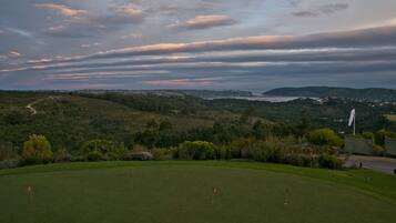 Un parcours de golf offrant une vue panoramique sur des collines et un plan d’eau situé au loin.