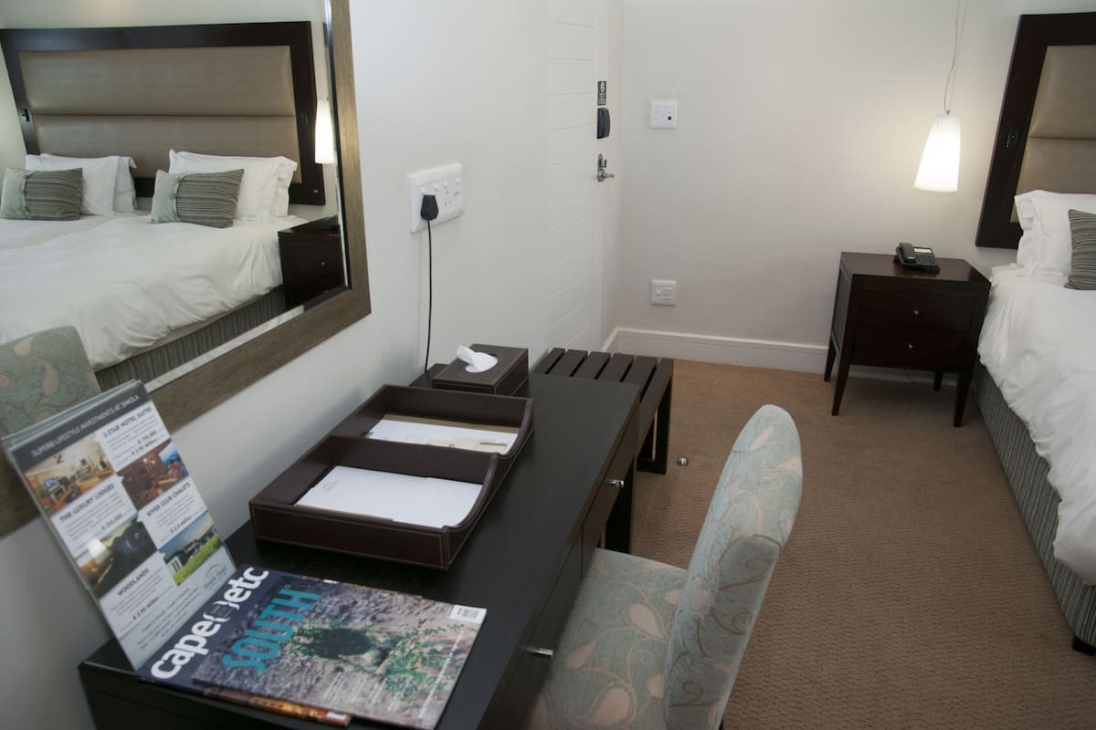 A hotel room with a bed, bedside table, desk with a chair, and a large mirror.