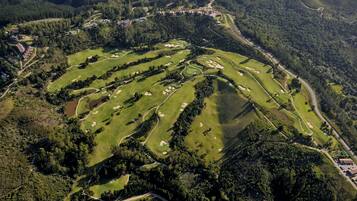 Vue aérienne d’un terrain de golf comportant plusieurs trous, entouré d’une forêt dense et de bâtiments résidentiels.