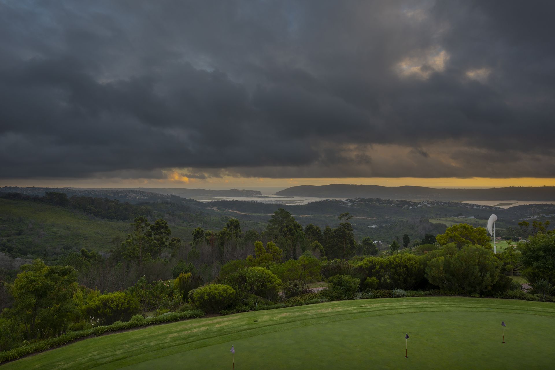 A golf course with a view of distant hills and a cloudy sky.