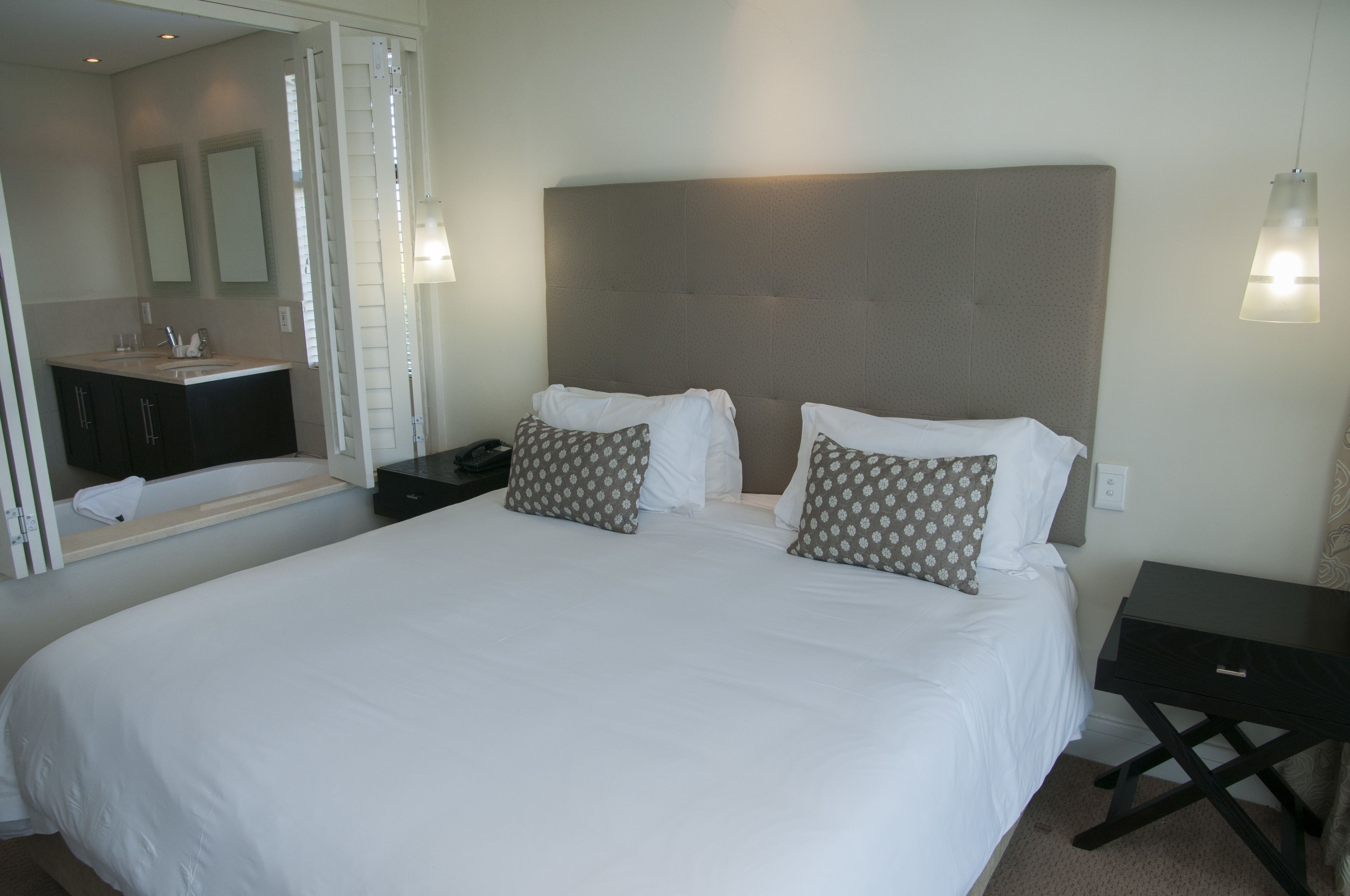 Camera d'albergo con un letto grande, due comodini, uno specchio e un bagno con lavandino e specchio.