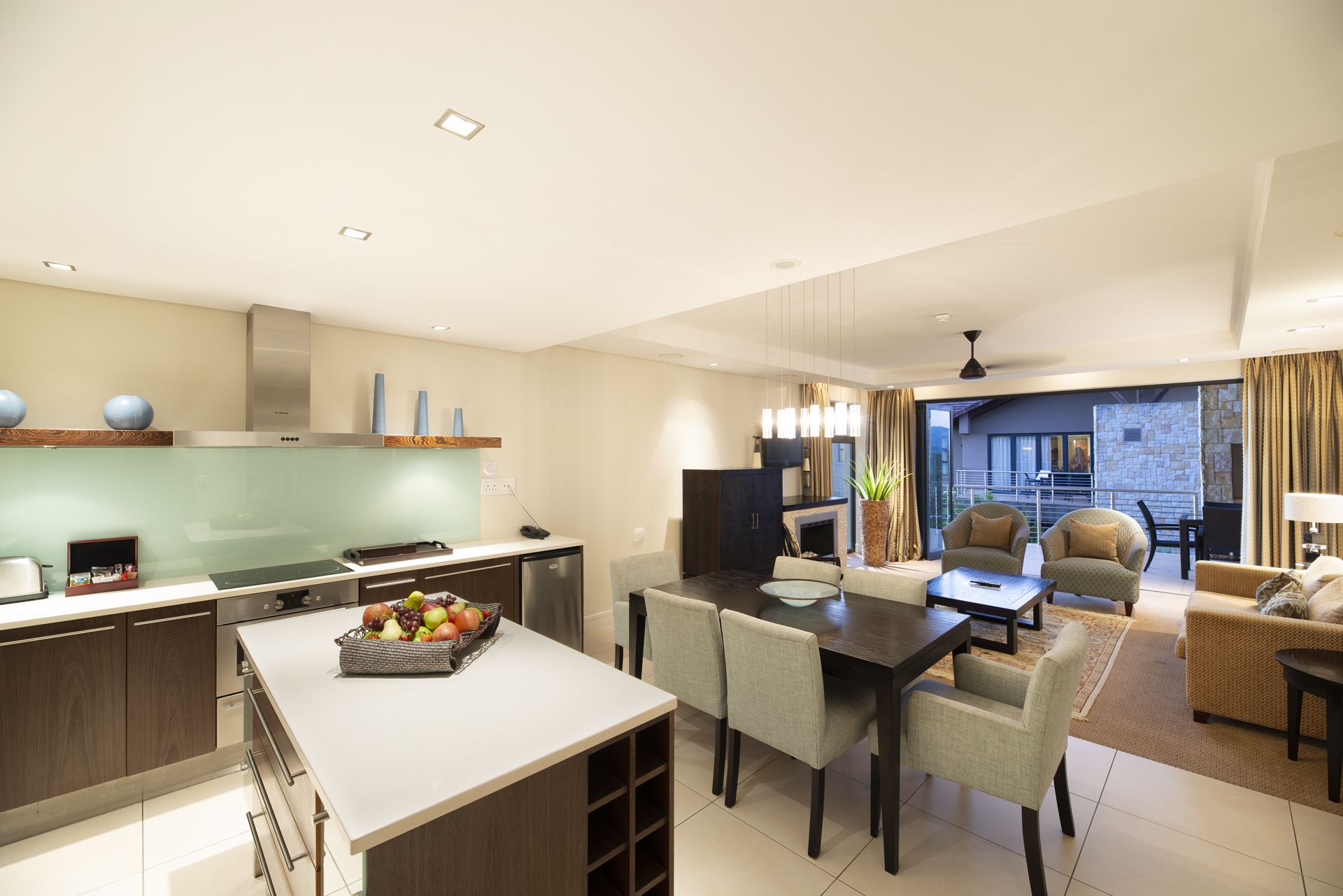 Cozinha moderna com área de refeições, sala de estar com sofá e poltronas, e vista para a varanda.