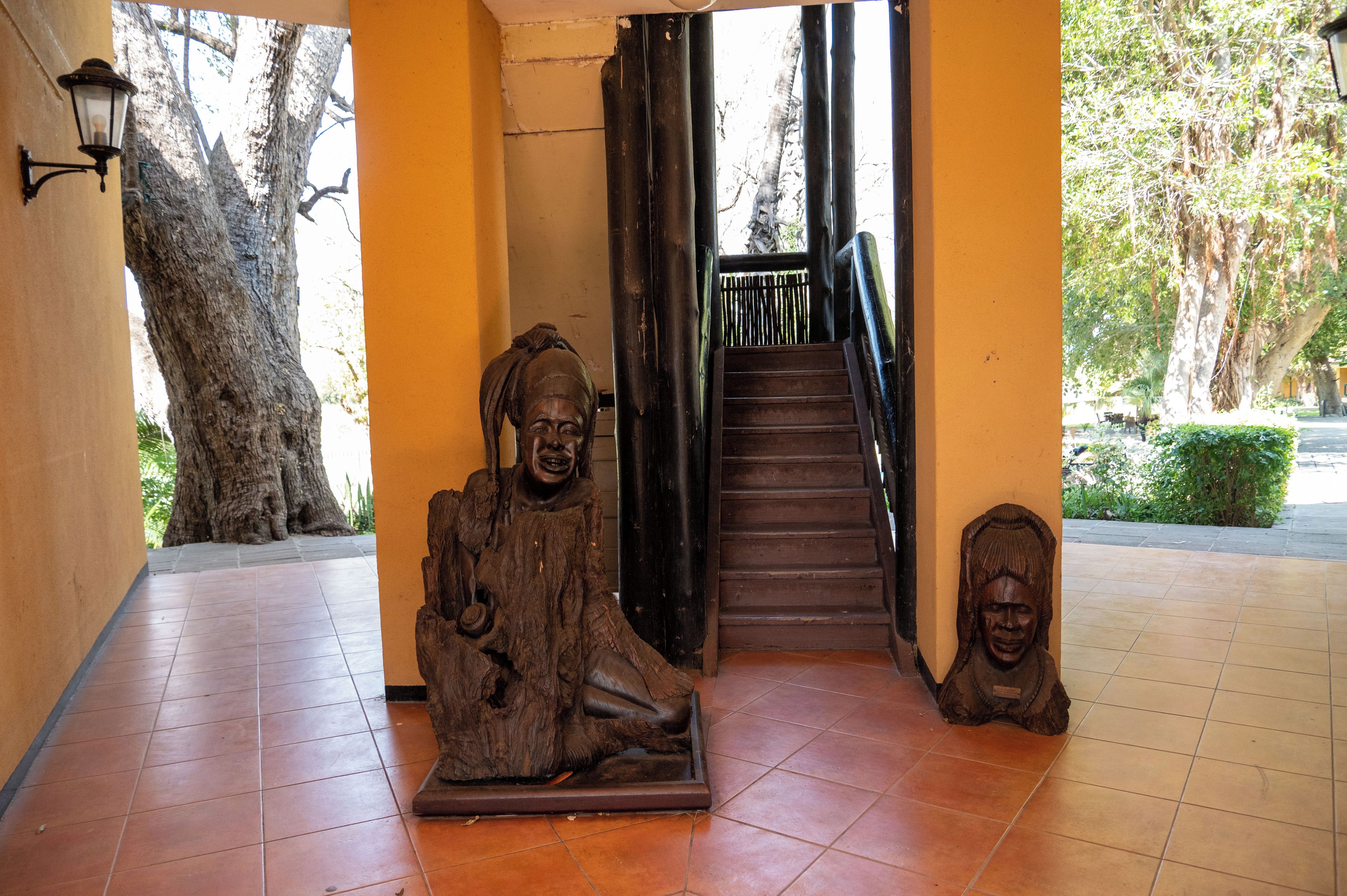 A staircase with a wooden handrail and a metal railing, flanked by two wooden sculptures.